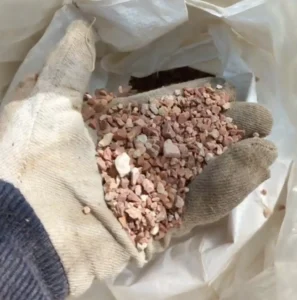 A person holding a hand full of granular red zeolite
